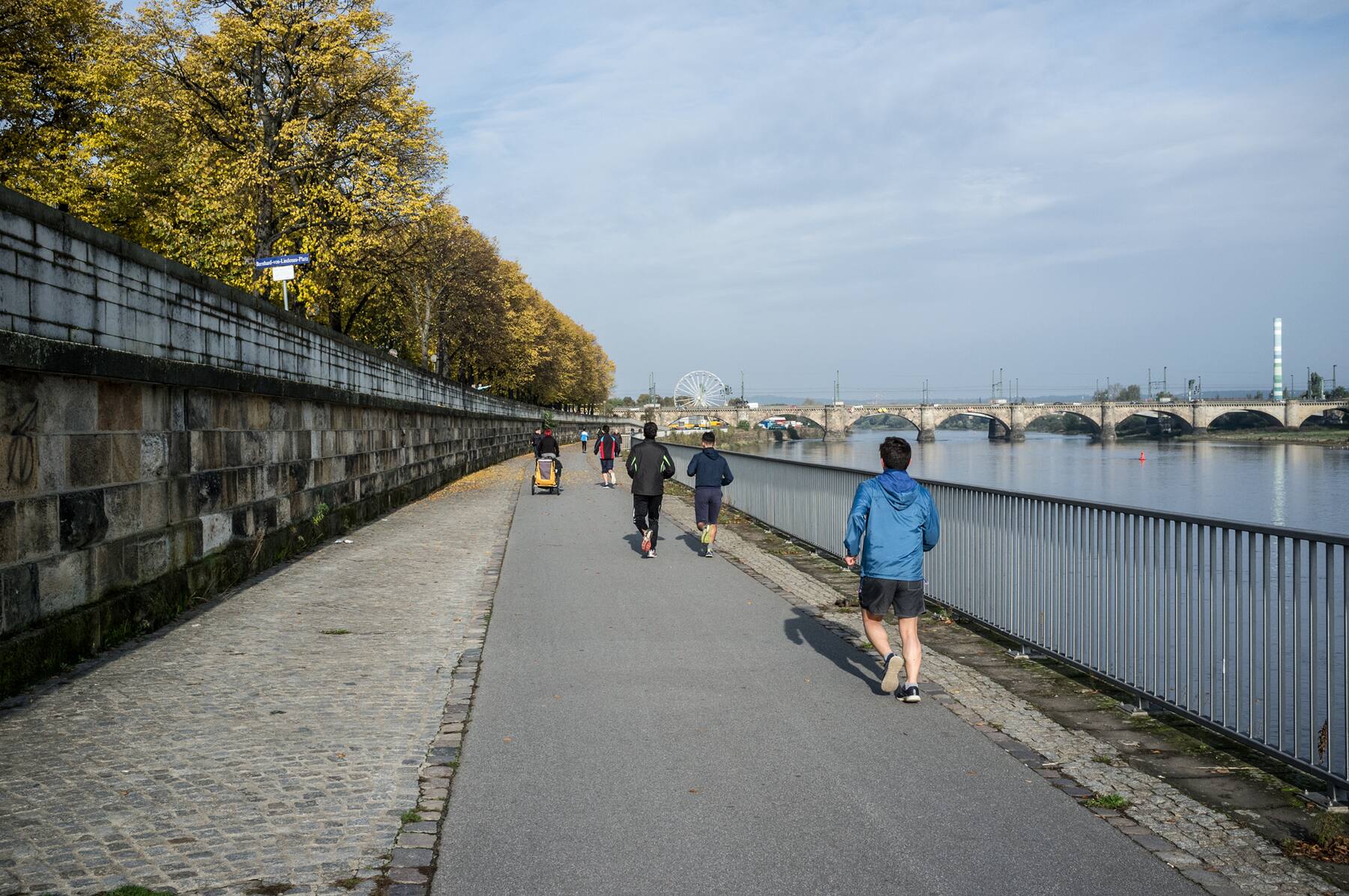Riverside path with joggers and a distant ferris wheel